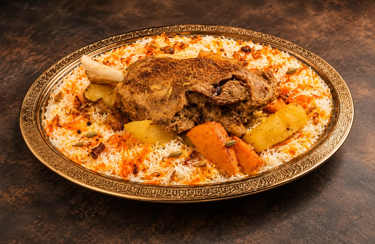Slow-roasted lamb with potato and carrot over saffron Mandi rice on an ornate brass platter